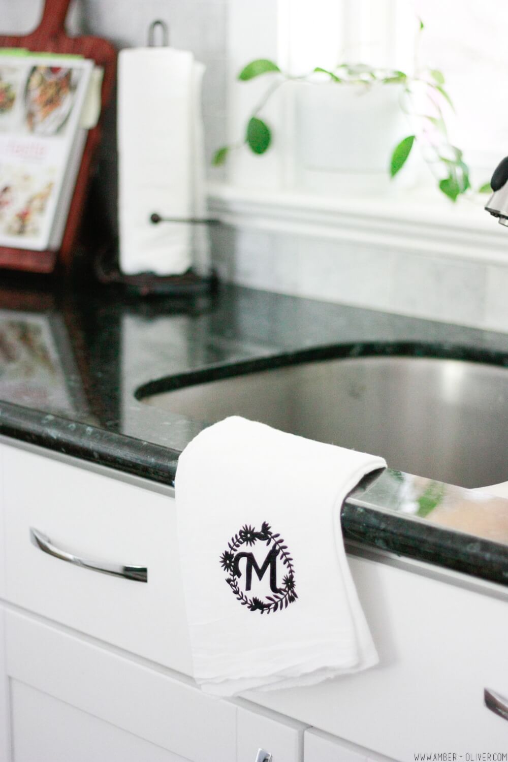 White handtowel hanging over a black sink and counter top with a monogram in black vinyl.