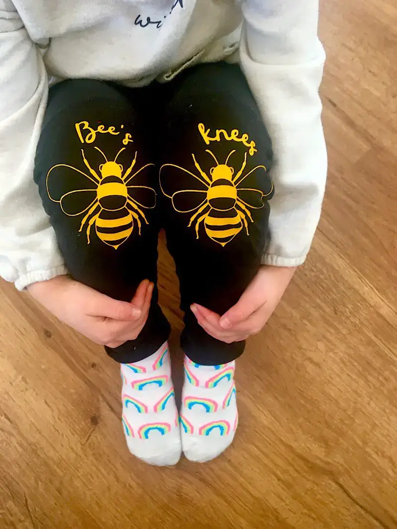 Child wearing black leggings with bees knees and cute bee images on each knee.