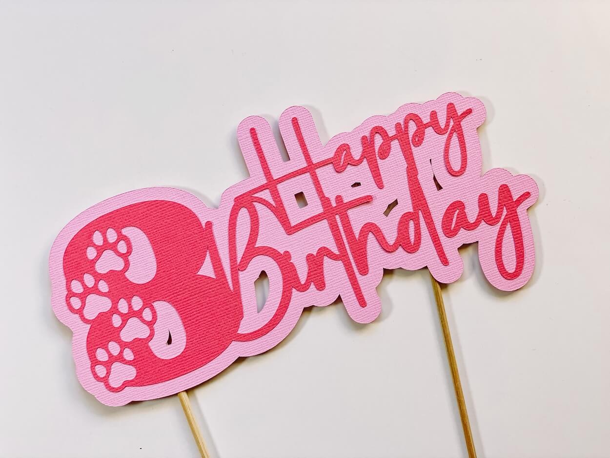8th birthday cake topper using pink cardstock with happy birthday and paw prints.