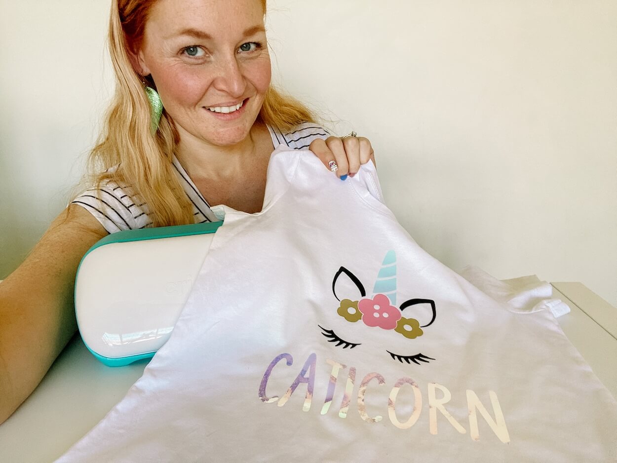 Woman holding caticorn tshirt next to a cricut joy cutting machine.