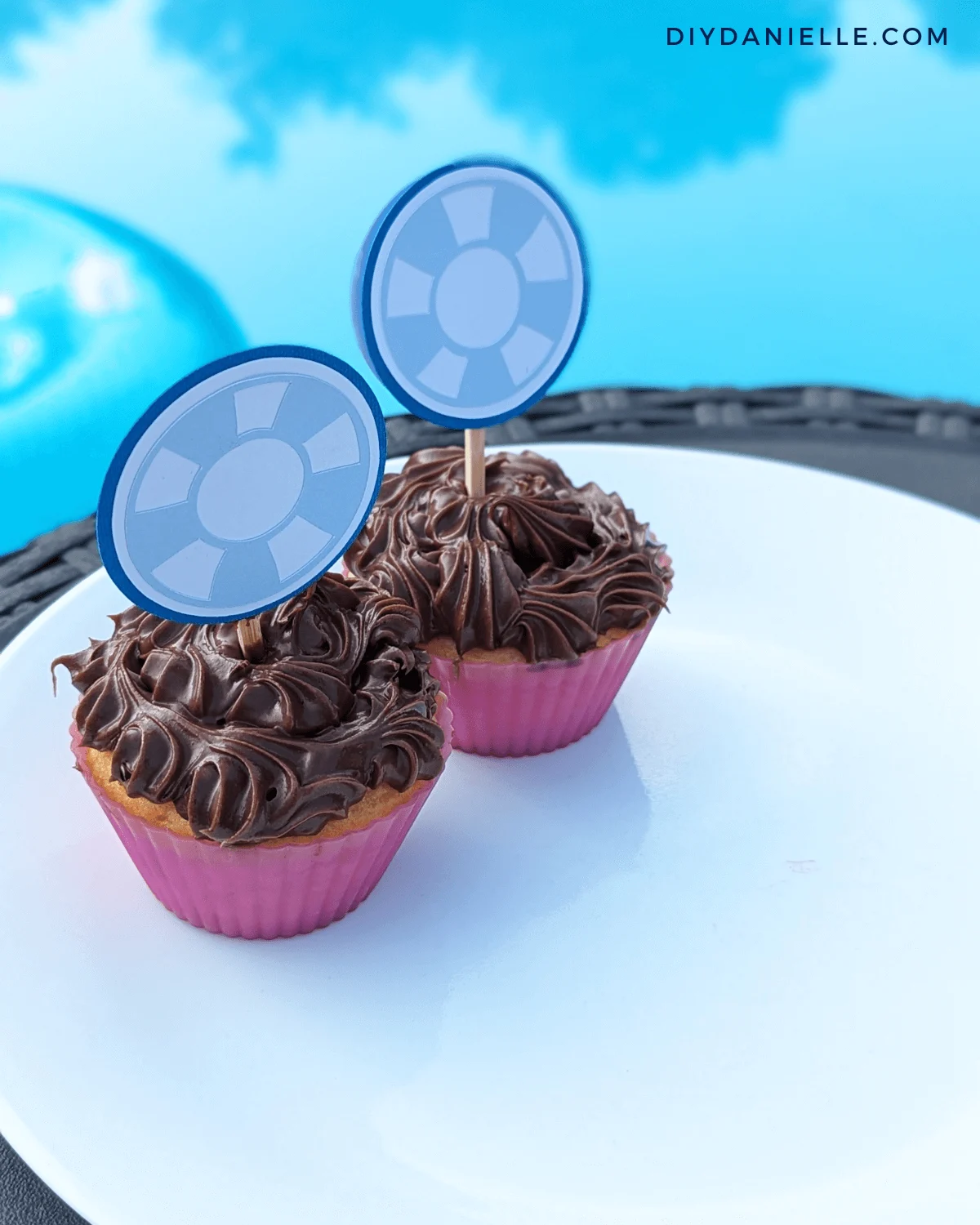 Beach ball cupcake toppers made with blue and white cardstock sticking out of 2 chocolate cupcakes.