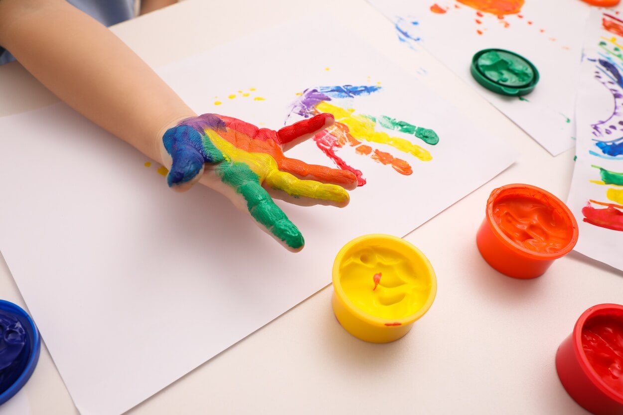 child with different coloured paints on hand doing handpainting on paper.