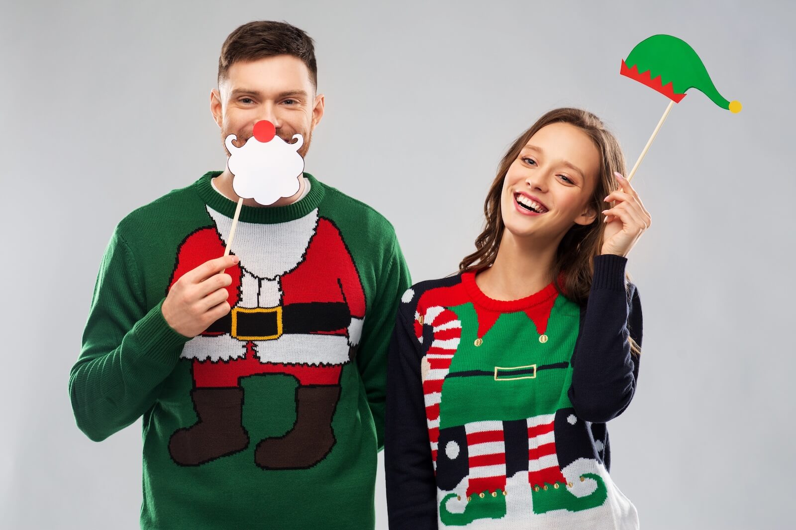 Man and woman wearing ugly christmas sweaters with photo props.